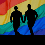 A picture of two men (Rudy Reyes, and Chris Hannifin) holding hands while running together. Behind waves an LGBTQ+ flag